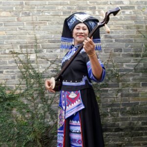 Zhuang woman in vibrant traditional dress holding a folk instrument outdoors.